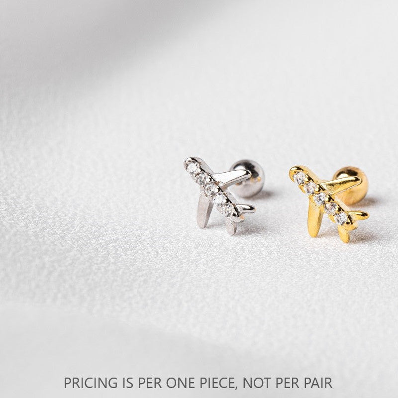 Two pieces of body jewelry resembling airplanes with one piece in silver and the other in gold finish, placed against a light background. The text clarifies that pricing is per one piece, not per pair.