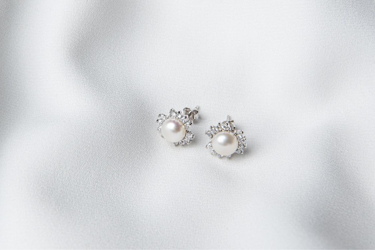 A pair of silver, pearl and cubic zirconia stud earrings on a white background.