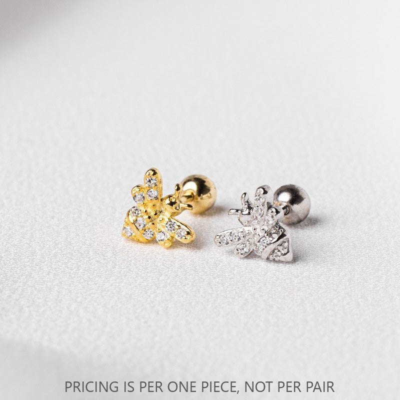 A pair of gold and silver colored stud earrings in the shape of a bee, placed on a white textured surface.