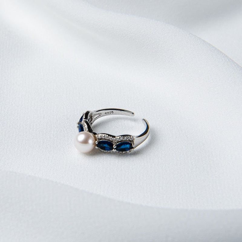 An adjustable size ring with a polished finish, made of sterling silver and blue cubic zirconia, featuring a white freshwater pearl.