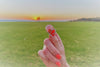 A pair of heart-shaped stud earrings made of sterling silver, held by a womans hand with a sunset in the background