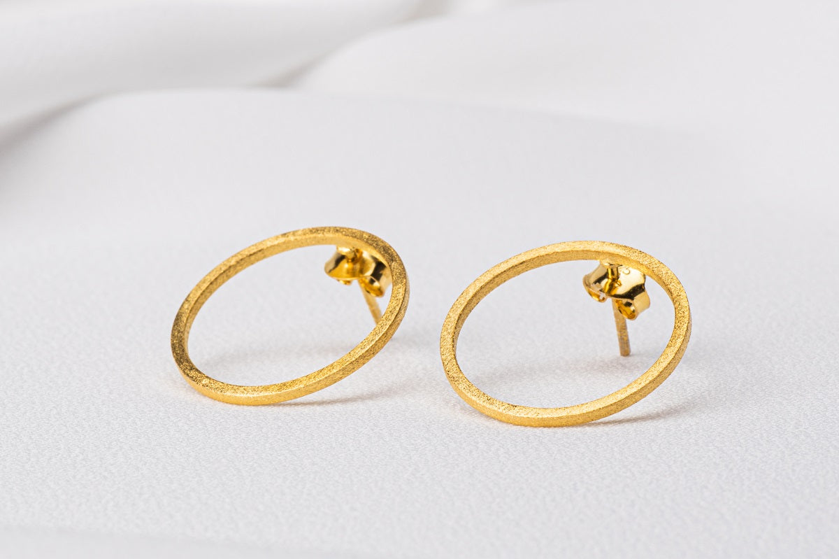 Two gold circle shaped earrings on a white background