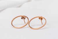 Two rose gold circle shaped earrings on a white background