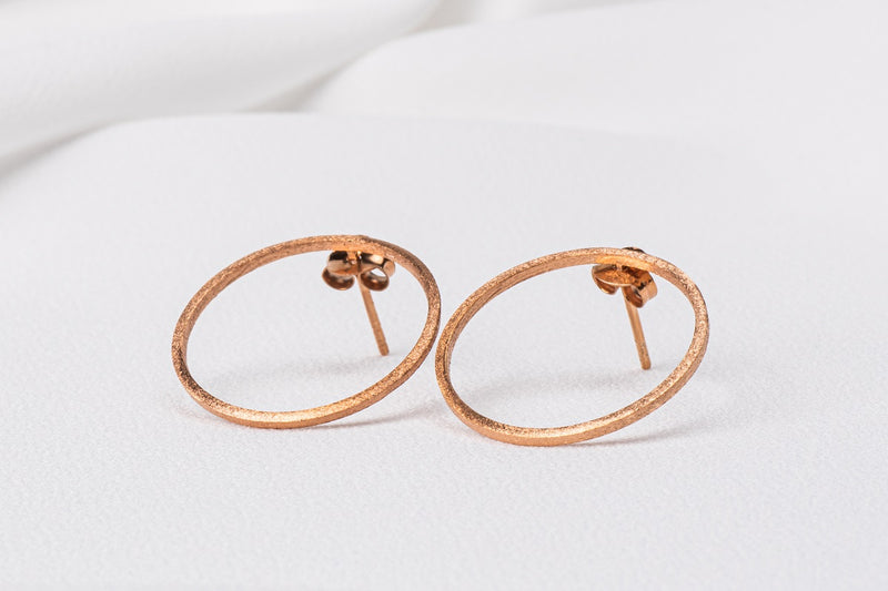 Two rose gold circle shaped earrings on a white background
