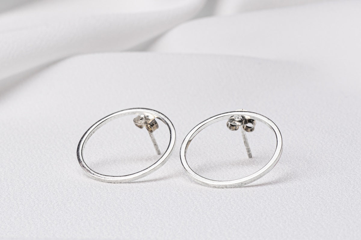 Two silver circle shaped earrings on a white background
