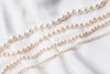 A white pearl choker necklace with a sterling silver chain, displayed on a white fabric