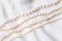 A white pearl choker necklace with a sterling silver chain, displayed on a white fabric