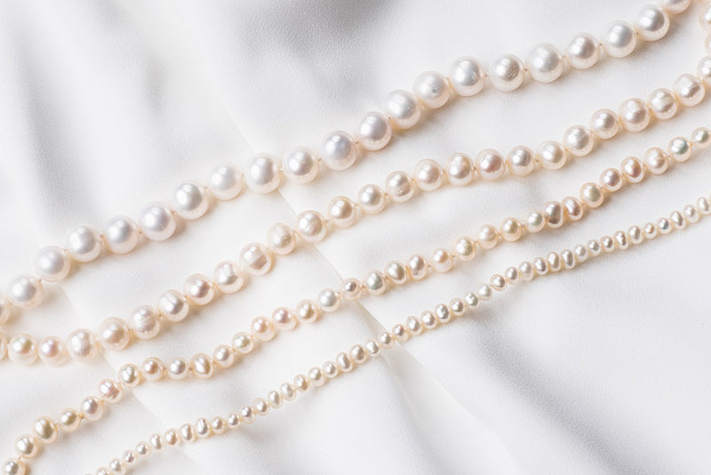 A white pearl choker necklace with a sterling silver chain, displayed on a white fabric