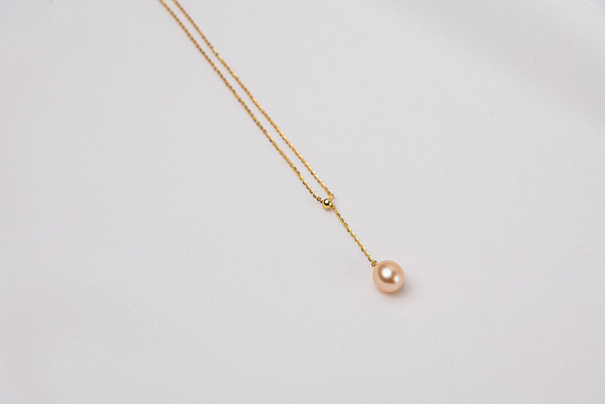A classic drop pearl necklace with a gold chain and a champagne pearl pendant, displayed on a neutral background.