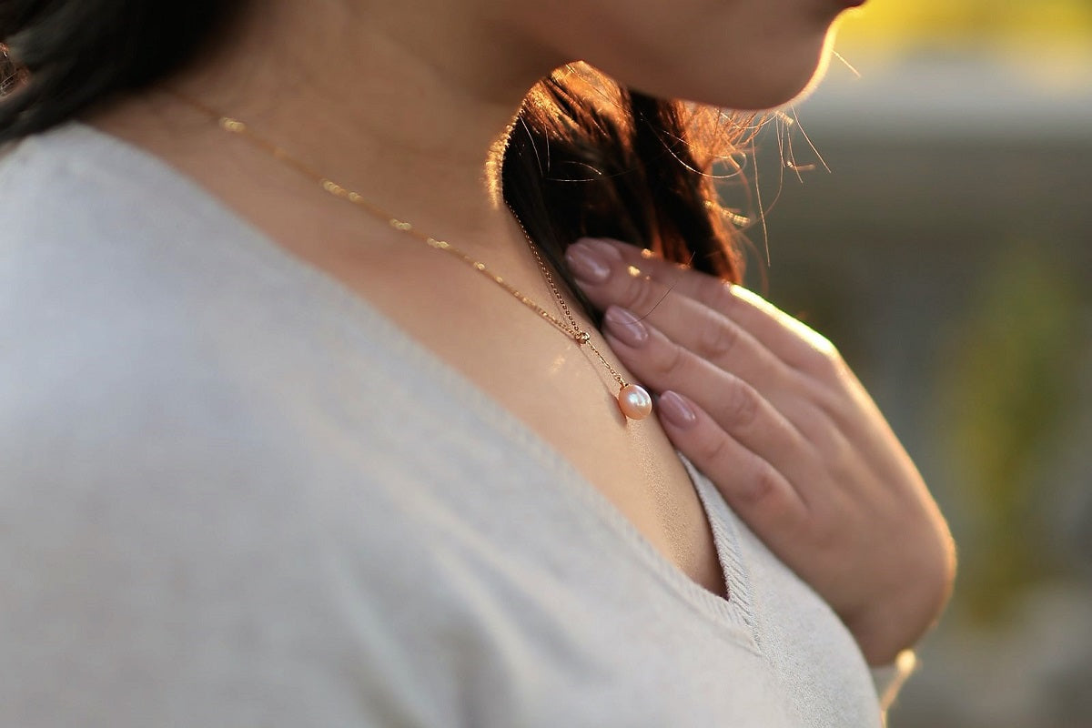A women wearing a classic drop pearl necklace with a gold chain and a champagne pearl pendant.