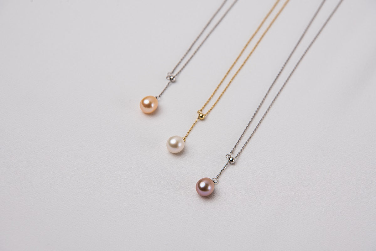 A classic drop pearl necklace with a gold and silver chain and a white ,champagne and lavender pearl pendant, displayed on a neutral background.