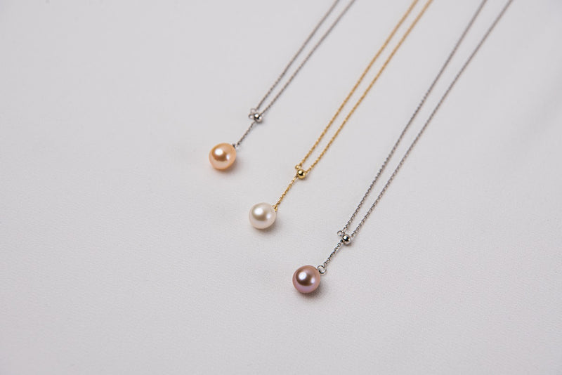 A classic drop pearl necklace with a gold and silver chain and a white ,champagne and lavender pearl pendant, displayed on a neutral background.