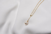 A classic drop pearl necklace with a gold chain and a white pearl pendant, displayed on a neutral background.