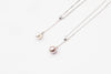 A classic drop pearl necklace with a silver chain and a white and lavender pearl pendant, displayed on a neutral background.
