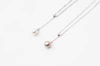 A classic drop pearl necklace with a silver chain and a white and lavender pearl pendant, displayed on a neutral background.