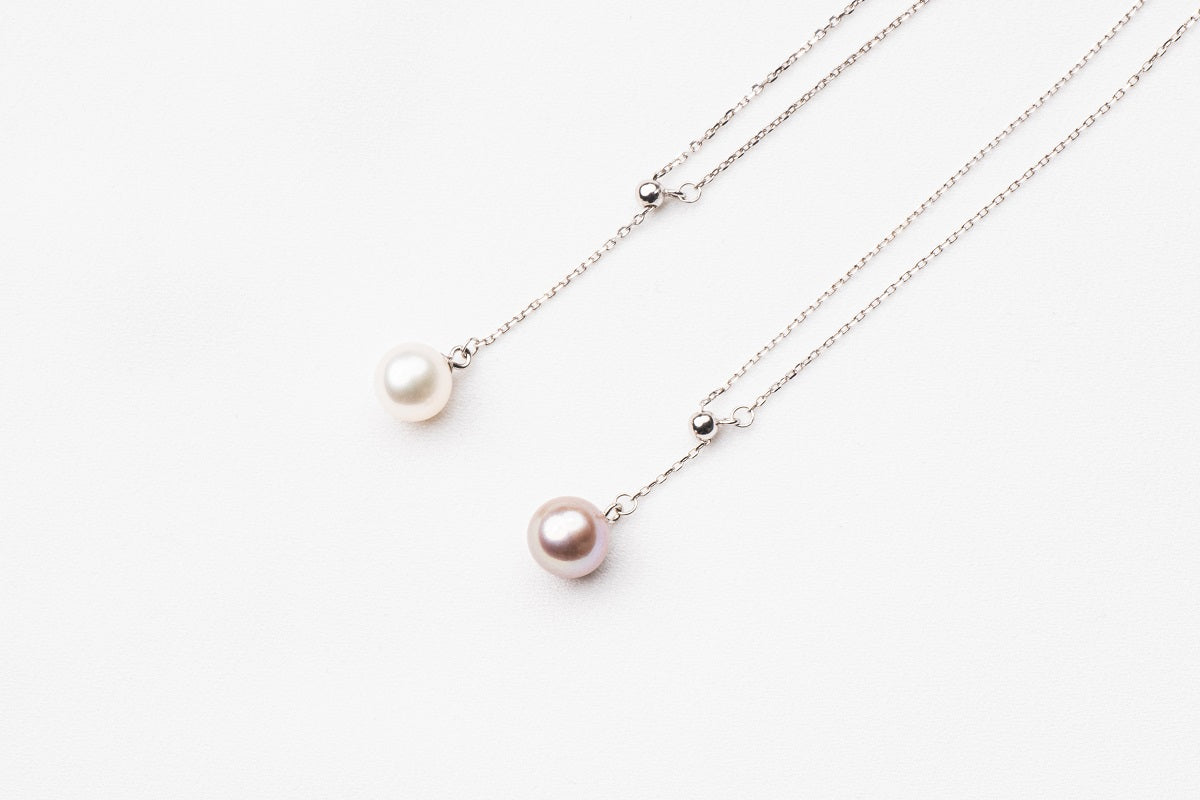 A classic drop pearl necklace with a silver chain and a white and lavender pearl pendant, displayed on a neutral background.
