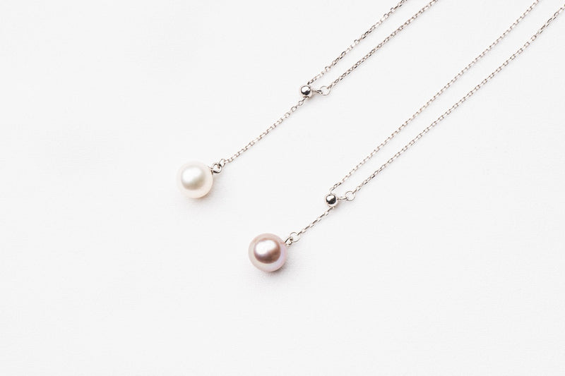 A classic drop pearl necklace with a silver chain and a white and lavender pearl pendant, displayed on a neutral background.