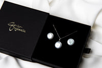 A sterling silver necklace with a white pearl pendant and a box chain style, and matching earrings displayed in a gift box on a white boackground