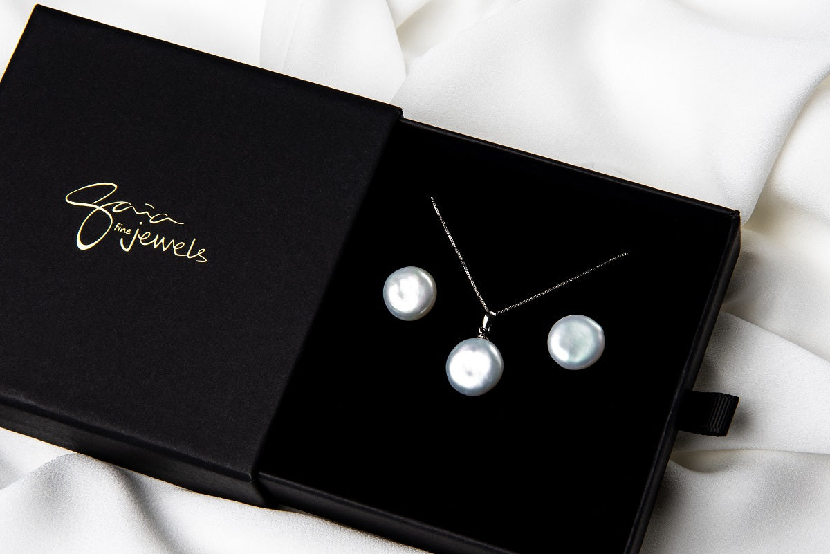 A sterling silver necklace with a white pearl pendant and a box chain style, and matching earrings displayed in a gift box on a white boackground