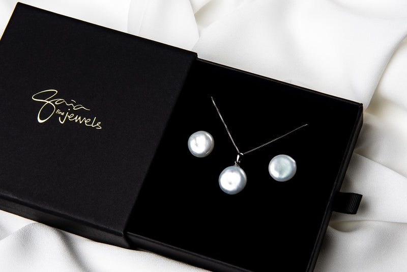 A sterling silver necklace with a white pearl pendant and a box chain style, and matching earrings displayed in a gift box on a white boackground