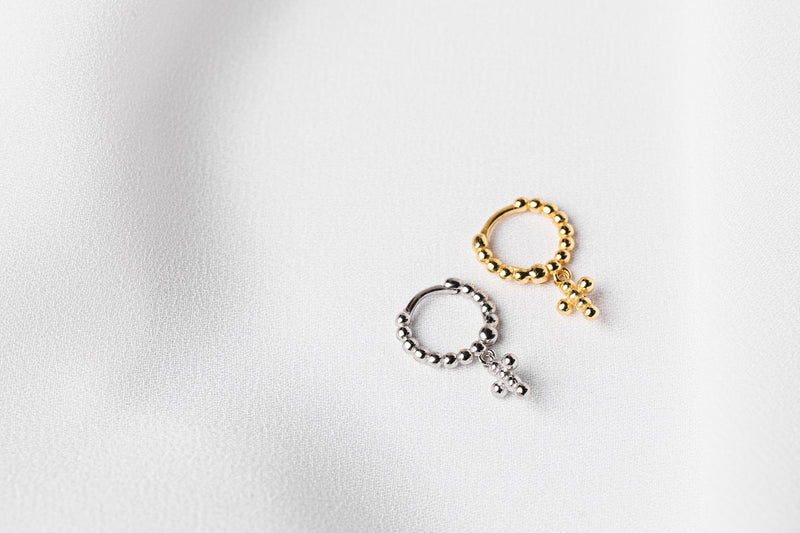 A pair of hoop earrings, one sterling silver and one gold vermeil with bubble and cross patterns on a white fabric background.