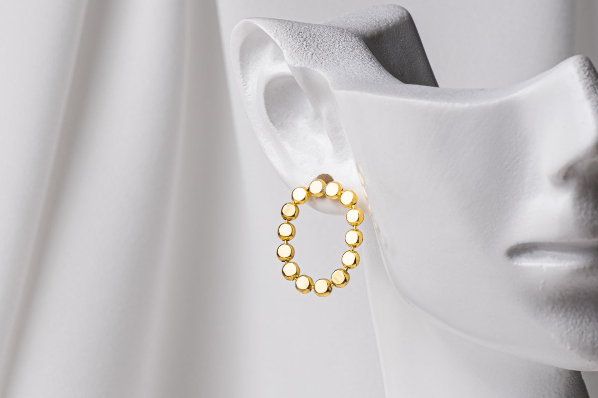 A pair of gold vermeil stud earrings, displayed on a metal earring stand against a white background
