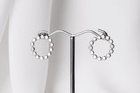 A pair of silver stud earrings, displayed on a metal earring stand against a white background