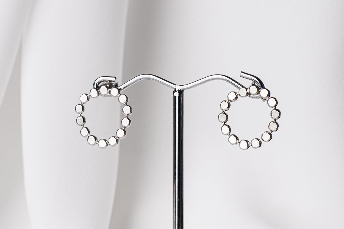 A pair of silver stud earrings, displayed on a metal earring stand against a white background