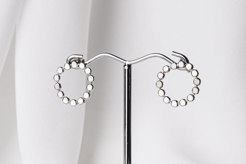A pair of silver stud earrings, displayed on a metal earring stand against a white background