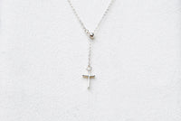 A silver chain drop necklace with a small silver cross pendant on a white background
