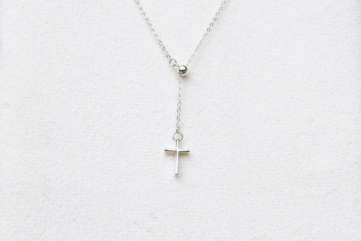 A silver chain drop necklace with a small silver cross pendant on a white background