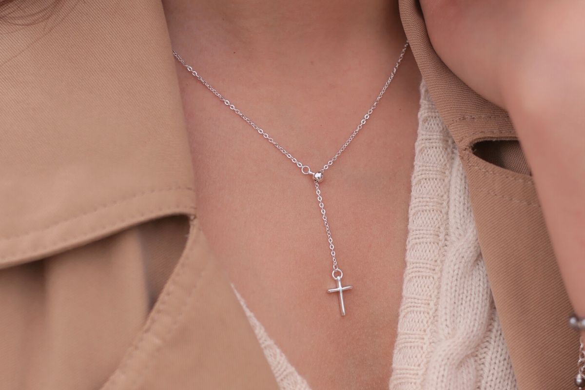 A silver chain drop necklace with a small silver cross pendant worn by a woman