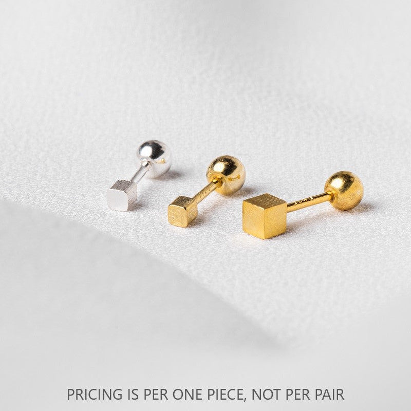Two gold and one silver piercing in the shape of a cube on a white cloth surface