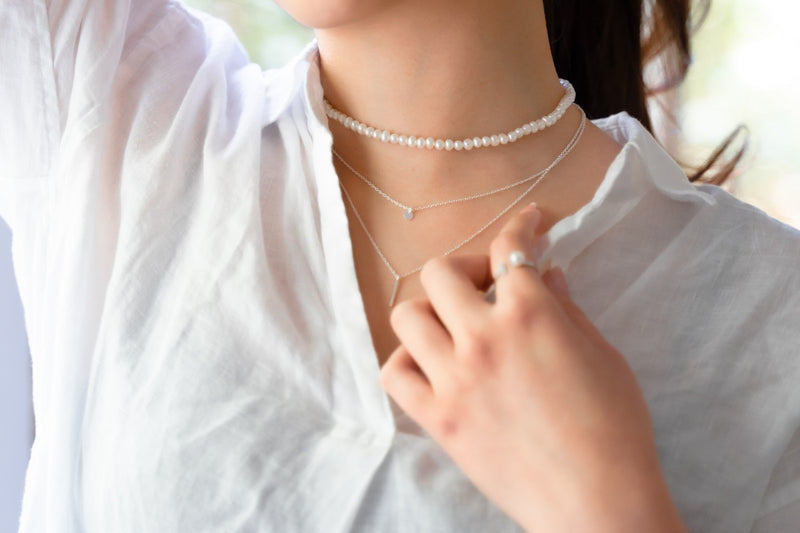 A woman wearing a white dress and a choker 4 mm pearl necklace and sterling silver 925 layer necklace