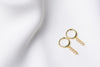 A pair of gold vermeil hoop earrings with a dangle cubic zirconias on a white fabric surface.