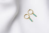 A pair of gold vermeil hoop earrings with a dangle of baby blue stones on a white fabric surface.