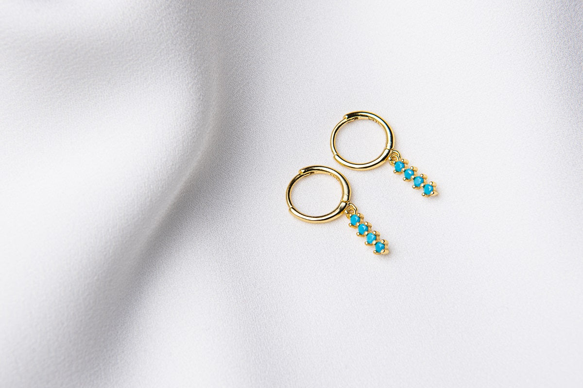 A pair of gold vermeil hoop earrings with a dangle of baby blue stones on a white fabric surface.