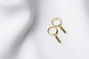 A pair of gold vermeil hoop earrings with a dangle of black cubic zirconias on a white fabric surface.