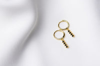 A pair of gold vermeil hoop earrings with a dangle of black cubic zirconias on a white fabric surface.