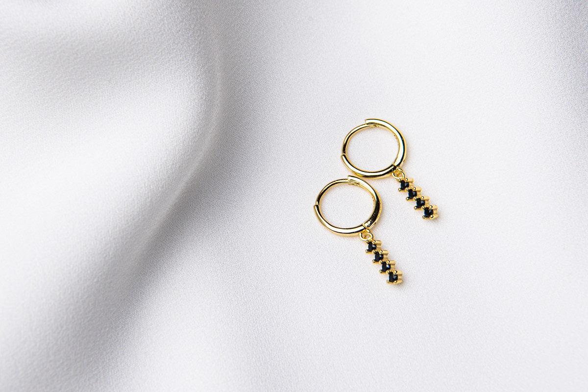 A pair of gold vermeil hoop earrings with a dangle of black cubic zirconias on a white fabric surface.