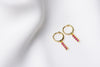 A pair of gold vermeil hoop earrings with a dangle of pink cubic zirconias on a white fabric surface.