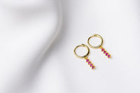 A pair of gold vermeil hoop earrings with a dangle of pink cubic zirconias on a white fabric surface.