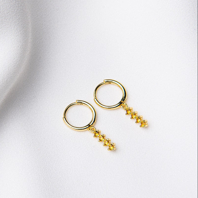 A pair of gold vermeil hoop earrings with a dangle of yellow cubic zirconias on a white fabric surface.