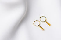 A pair of gold vermeil hoop earrings with a dangle of yellow cubic zirconias on a white fabric surface.