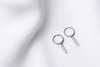 A pair of silver hoop earrings with a dangle of cubic zirconias on a white fabric surface.