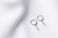 A pair of silver hoop earrings with a dangle of cubic zirconias on a white fabric surface.