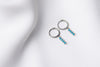A pair of silver hoop earrings with a dangle of baby blue stones on a white fabric surface.
