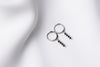A pair of silver hoop earrings with a dangle of black cubic zirconias on a white fabric surface.