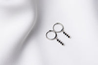 A pair of silver hoop earrings with a dangle of black cubic zirconias on a white fabric surface.