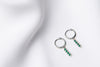 A pair of silver hoop earrings with a dangle of green cubic zirconias on a white fabric surface.